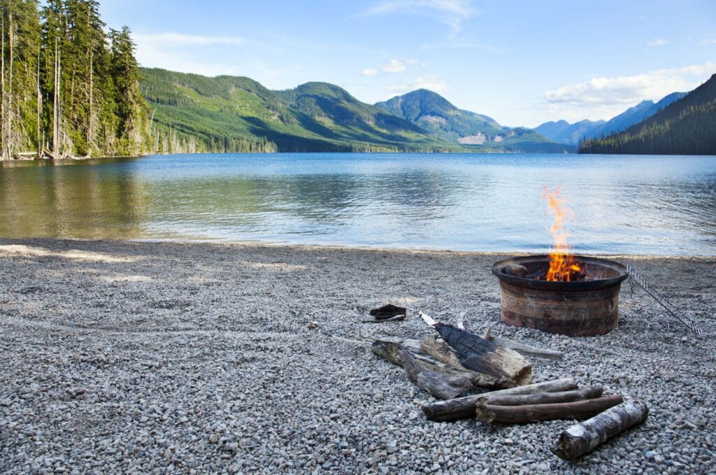 campfire in front of lake with mountains in the background