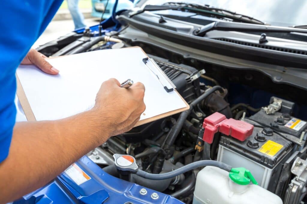 the arm of a mechanic holding a clipboard while checking the engine of a car
