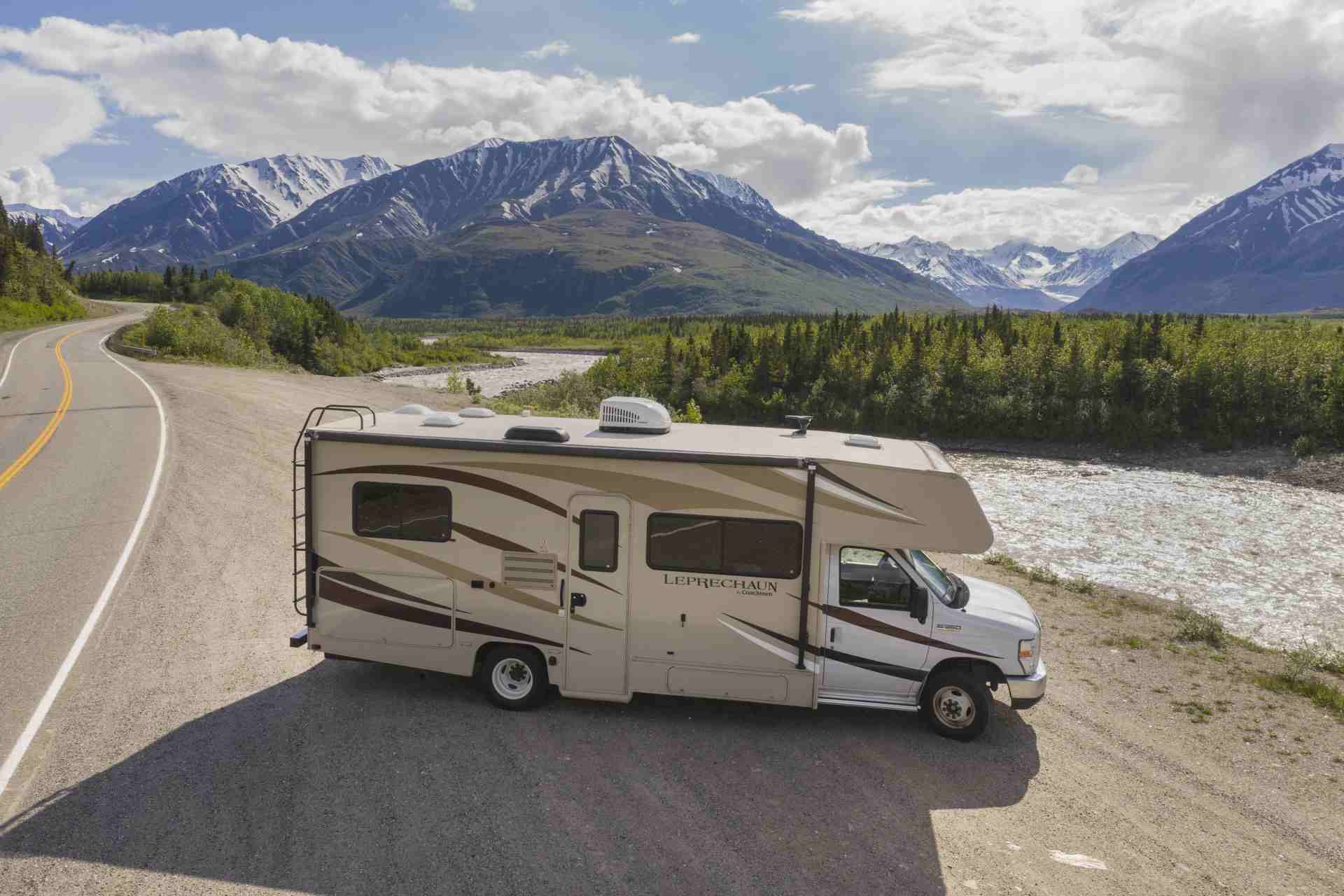 Motorhome on a gravel lot with a road on the left, a river on the right and mountains in the background
