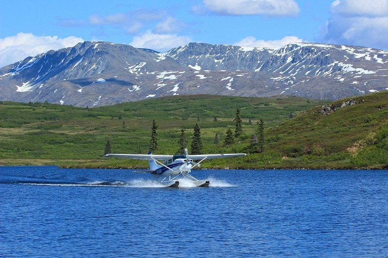 A float plane landing on a blue lake in front of Caribou Lodge Alaska
