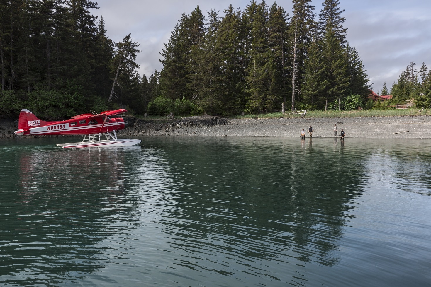 a red floatplane landing at the shore