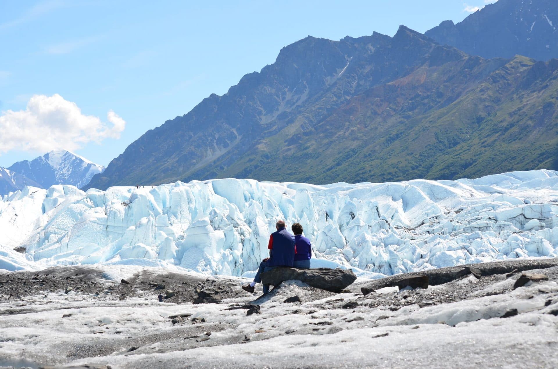 couple sitting in front of a large glacier