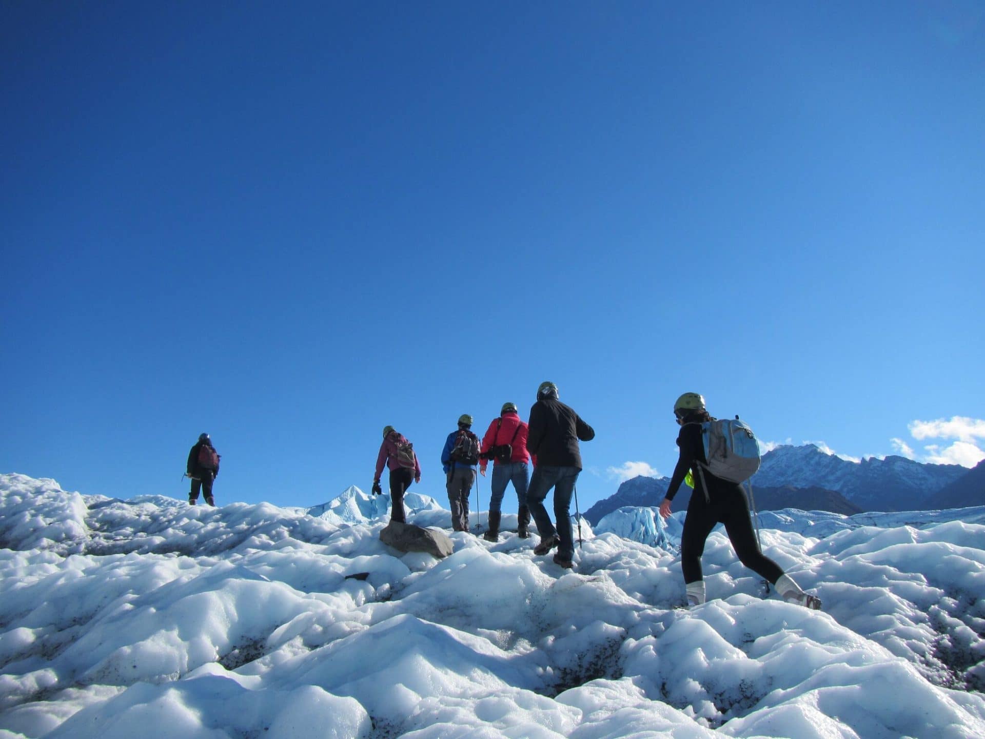 6 people walking on a glacier in a row