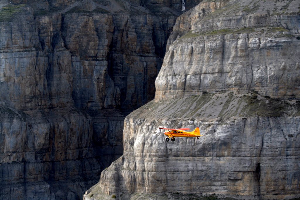 small orange plane in front of a massive rock