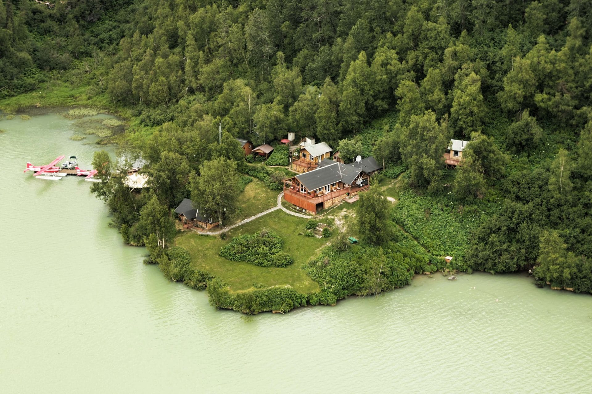 a lodge on the coast from high above, green water and trees surrounding the ldoge