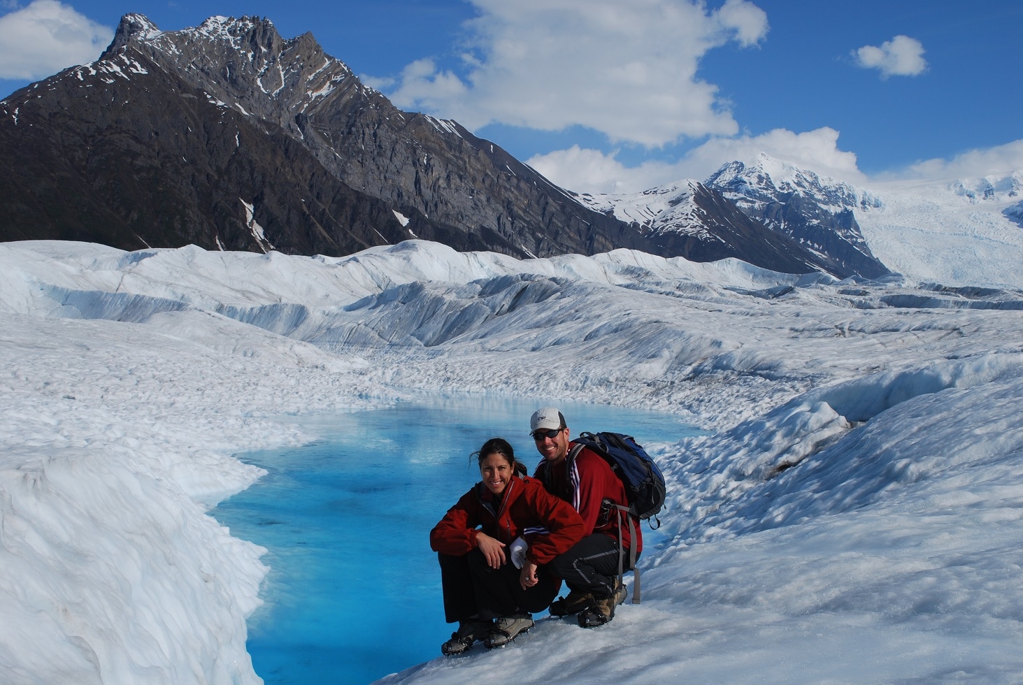 a couple sitting at a blue pond on a glacier