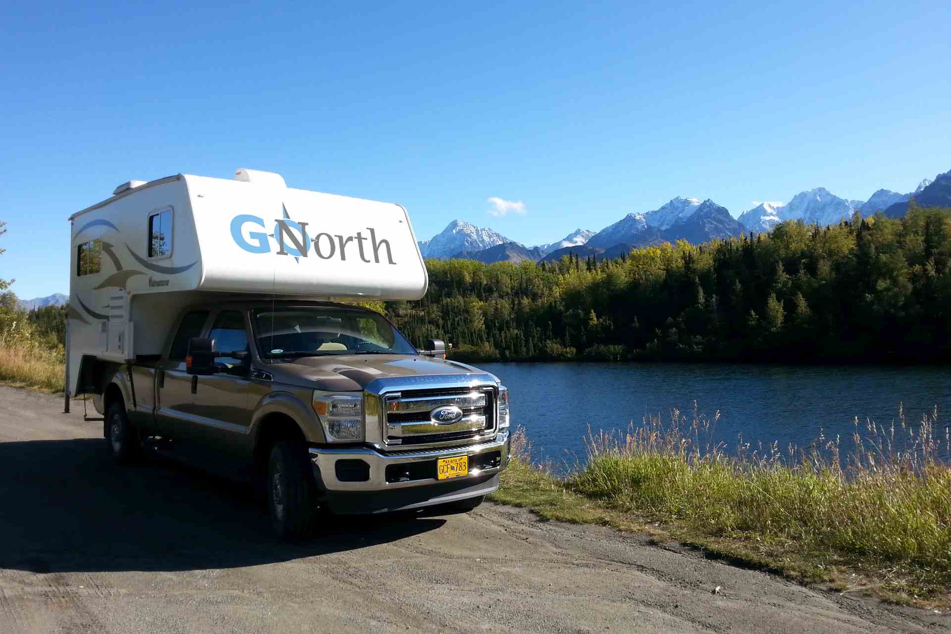 Truck Camper next to a lake with mountains in the background