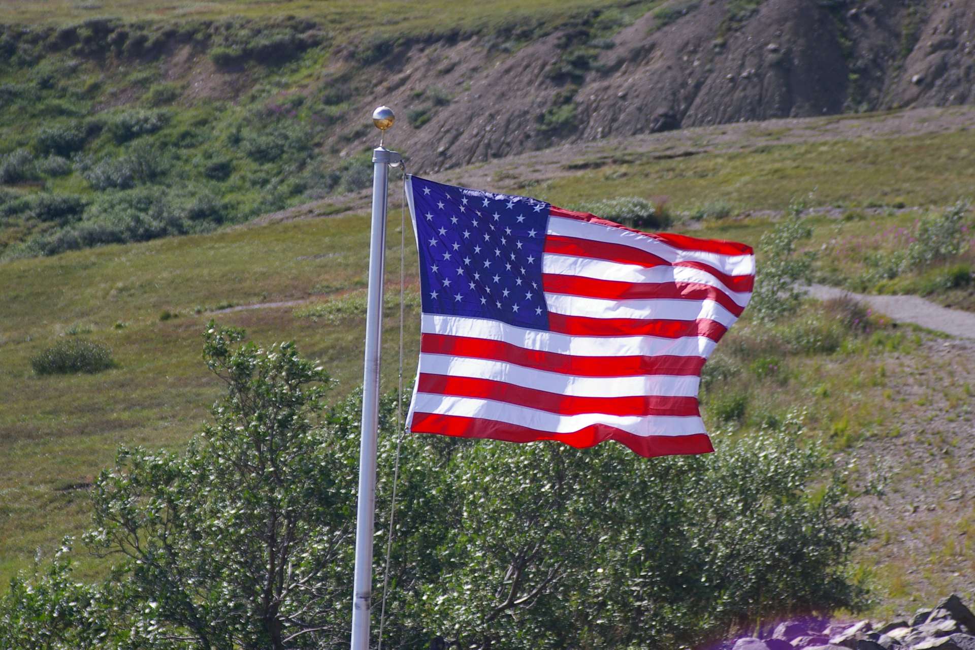 US Flag blowing in the wind during daylight with a green hill in the background