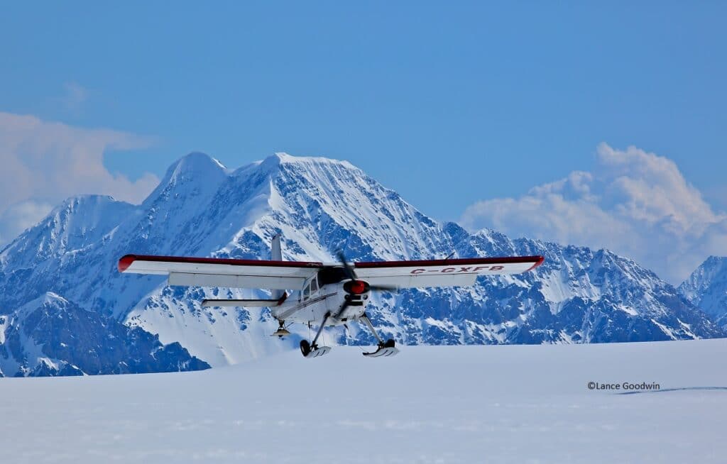 small skiplane landing on a glacier surrounded by snowcapped mountains