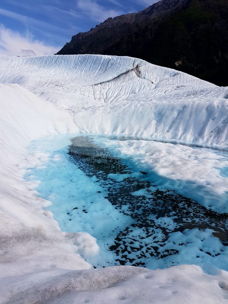 Glacial blue pool with ice in the background during daylight
