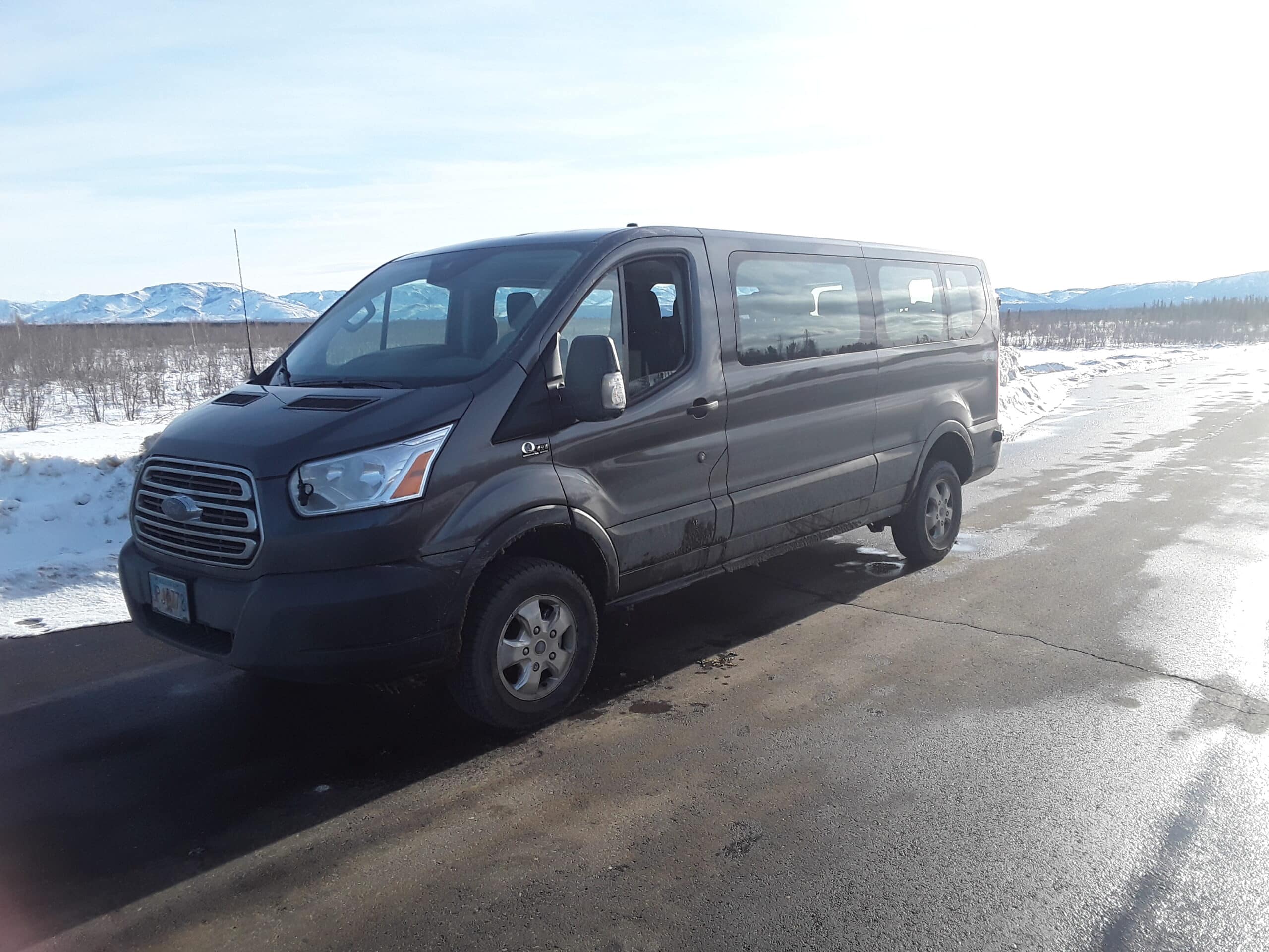 lateral view of a black passenger van during daylight on a paved road with a mountain in the background.